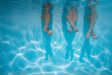 Wall Mural - close up of friends, family legs underwater in the swimming pool with copy space