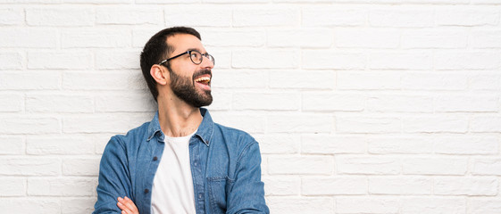 Handsome man with beard over white brick wall happy and smiling