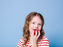 Beautiful Young Girl Is Posing With Red Apple In Front Of Blue Background