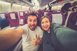 happy handsome couple taking a selfie on the airplane during flight around the world. They are a man and a woman, smiling and looking at camera. Travel, happiness and lifestyle concepts.