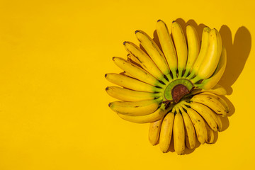 Wall Mural - ripe trendy ready to eat ugly bunch of mini bananas with black dots on yellow surface