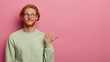 © WHstudio Leushin N - Bearded red head adult man points with thumb to right side on copy space, shows advertisement or promo, has satisfied curious face expression, wears casual clothes, isolated over pink background