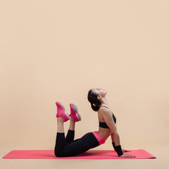 Young attractive girll, a brunette, is lies in a cobra pose with knees bent, doing stretching on a pink yoga mat.