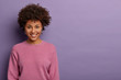 © wayhome.studio  - Portrait of lovely glad woman has Afro hair, smiles joyfully, gets pleasant news, gazes at camera cheerful, expresses upbeat emotions, models against purple background. Free space for your advert