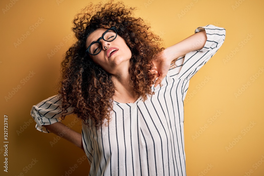 Young beautiful woman with curly hair and piercing wearing striped shirt and glasses stretching back, tired and relaxed, sleepy and yawning for early morning - obrazy, fototapety, plakaty 