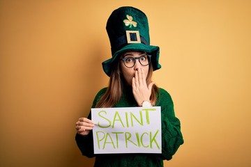 Sticker - Young beautiful woman wearing green hat holding banner on saint patricks day celebration cover mouth with hand shocked with shame for mistake, expression of fear, scared in silence, secret concept