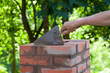 Masonry works,  male hand working with a trowel, repairing a chimney from red bricks on a roof
