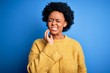 © Krakenimages.com - Young beautiful African American afro woman with curly hair wearing yellow casual sweater touching mouth with hand with painful expression because of toothache or dental illness on teeth. Dentist