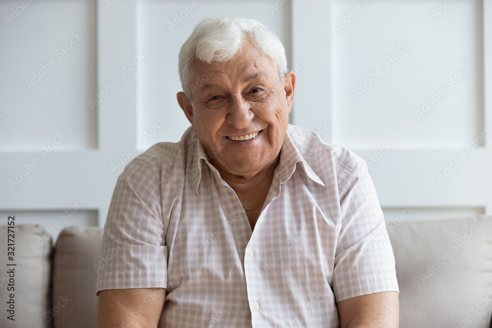 Headshot portrait of smiling mature man relaxing on sofa