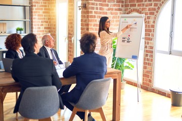 Group of business workers smiling happy and confident in a meeting. Working together looking at presentation using board and charts at the office.