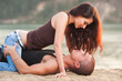 © ilyaska - Happy sexy brunette woman sitting on macho man on the sandy beach
