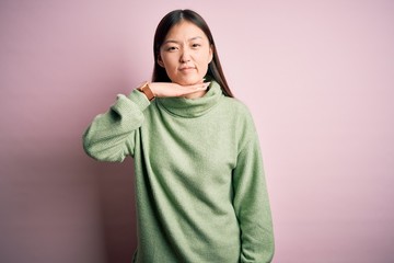 Canvas Print - Young beautiful asian woman wearing green winter sweater over pink solated background cutting throat with hand as knife, threaten aggression with furious violence