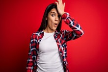Young Beautiful Brunette Woman Wearing Casual Shirt Standing Over Isolated Red Background Surprised With Hand On Head For Mistake, Remember Error. Forgot, Bad Memory Concept.