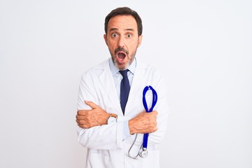 Poster - Middle age doctor man wearing coat holding stethoscope over isolated white background scared in shock with a surprise face, afraid and excited with fear expression