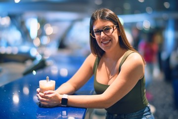 Young beautiful woman smiling happy and confident. Leaning on counter bar holding glass of coffee at restaurant