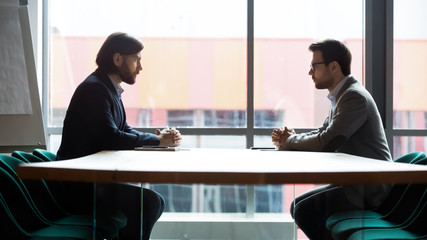 Two businessmen sitting opposite at table, confrontation and negotiation