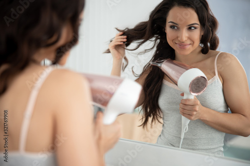 Cuadros en Lienzo Joyful young woman styling hair with hair dryer