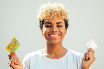 african american woman be lost in thought with one pack of condom and birth control pills choosing thinking white background studio