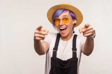 Hey, you are awesome! Portrait of amazed joyful glamour girl with violet hair in sunglasses and hat pointing to camera with two hands, choosing you. isolated on white background, indoor studio shot