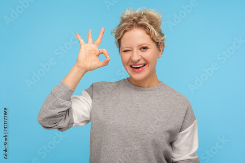 Cuadros en Lienzo Ok, everything is fine! Glad woman with short curly hair in sweatshirt smiling at camera and showing alright, okay gesture, winking at camera, agree to tricky plan