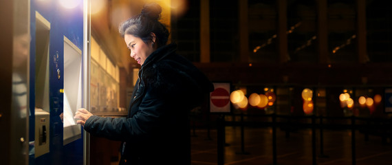 asain female woman  traveller withdrawing money from credit card at ATM nighttime with light bokeh background financial ideas concept