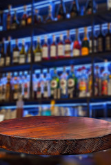 Wooden board on a background of bottles with alcohol. Old bar counter as layout for design. Workpiece for design. Empty place to advertise products. Blurred interior of the bar in the background.