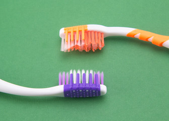 Two toothbrushes. White-orange and white-violet. On a green background. Brush heads