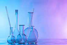 Chemical Glassware Is On The Table. Flasks And Test Tubes On A Lilac Background. Chemical Laboratory Equipment. Dishes For Demonstration Of Chemical Reactions