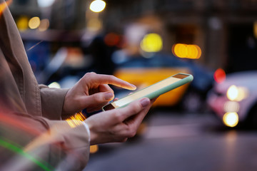 Wall Mural - Closeup photo of female hands with smartphone. Night street on background