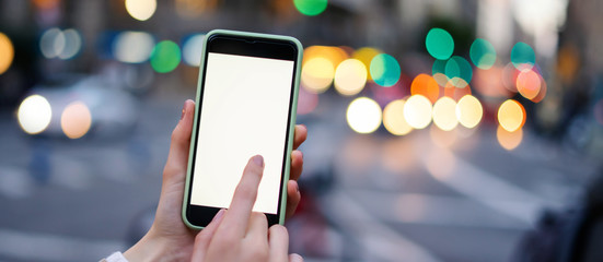 Wall Mural - Closeup photo of female hands holding modern smartphone with blank screen. Mockup ready for text message or content. Woman's hands with cellphone. Empty display. Night street, bokeh light