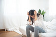 frustrated young asian woman in depressed emotion sitting on couch and head looking down,two hands cover ears in bedroom at home.