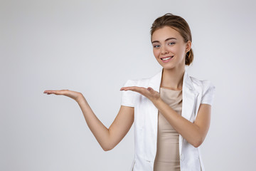 Wall Mural - smiling young business woman showing copyspace pointing on gray background. woman in white jacket showing space for text or your product