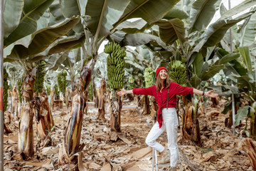Wall Mural - Beautiful plantation with a rich banana crop, portrait of a woman tourist or farmer dressed casually in red and white standing on the ladder. Concept of green tourism or exotic fruits producing