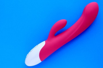 Sex toy for adult, design pink dildo vibrator isolated on blue background. Concept of sex, pleasure, present. Copy space.