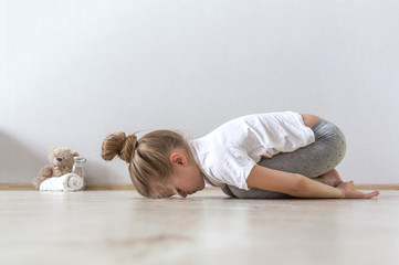 A little cute girl practices a yoga pose indoors. The child does yoga and gymnastic exercises.