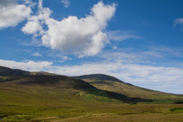 green irish hills with bright blue sky and puffy clouds casting deep shadows.