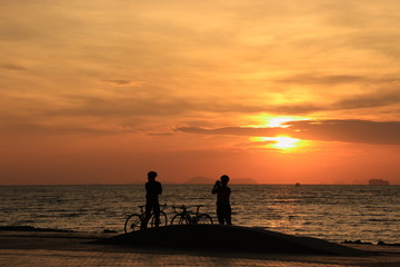 Wall Mural - The silhouette of lovers riding bicycles and watching and photographing the sunrise on the beach at dawn