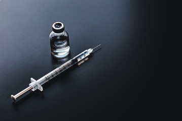 Medical syringe and ampoule with medicine on the black background, top view with copy space. Vaccination and virus protection concept