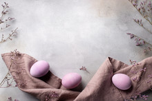 Purple Easter Eggs With Linen Napkin And Flowers On A Gray Concrete Background. Monochrome. Horizontal Image. Top View, Place For Text
