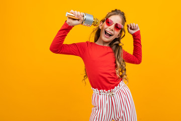 young girl comes off to music with a microphone in her hands on a yellow studio background with copy space