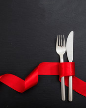 Valentine Day Dinner Table Setting. Fork And Knife Cutlery Tied With Red Ribbon On Black Background, Top View.