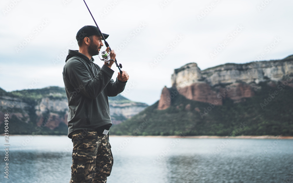 fisherman enjoy hobby with fishing rod on lake, person catch fish on background mountain, holiday relaxation fishery concept - obrazy, fototapety, plakaty 