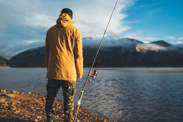 Wall Mural - fishery concept, fisherman enjoy relax hobby sport with fishing rod on evening lake, person catch fish on background blue sky