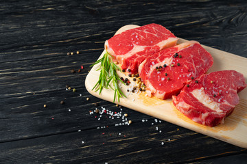 Wall Mural - Three pieces of juicy raw beef on a cutting board on a black wooden table background.