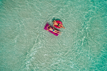 Wall Mural - .Summer holiday fashion concept - tanning couple at the beach on a turquoise sea shot from above. Top view from drone. Aerial view of slim woman and man sunbathing lying on a beach in Thailand.