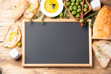 Wall Mural - Ciabatta bread, olive oil, thyme, green olives and chalkboard frame on a wooden background. Top view. Space for text.