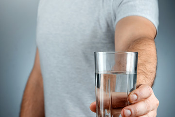 Glass cup with pure mineral water in male hands close-up on a gray background. medication, treatment, healthy drink.