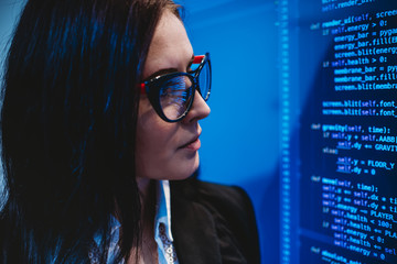Woman hacker with glasses looking at codes on screen