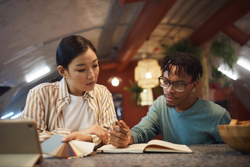 Wall Mural - portrait of two ethnic young people working on project together while sitting at table in office