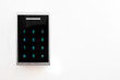 © a_khachatryan - Keypad electronic lock side view. Lock with black glossy front pane and blue dials placed on white wall. Copy space for text.